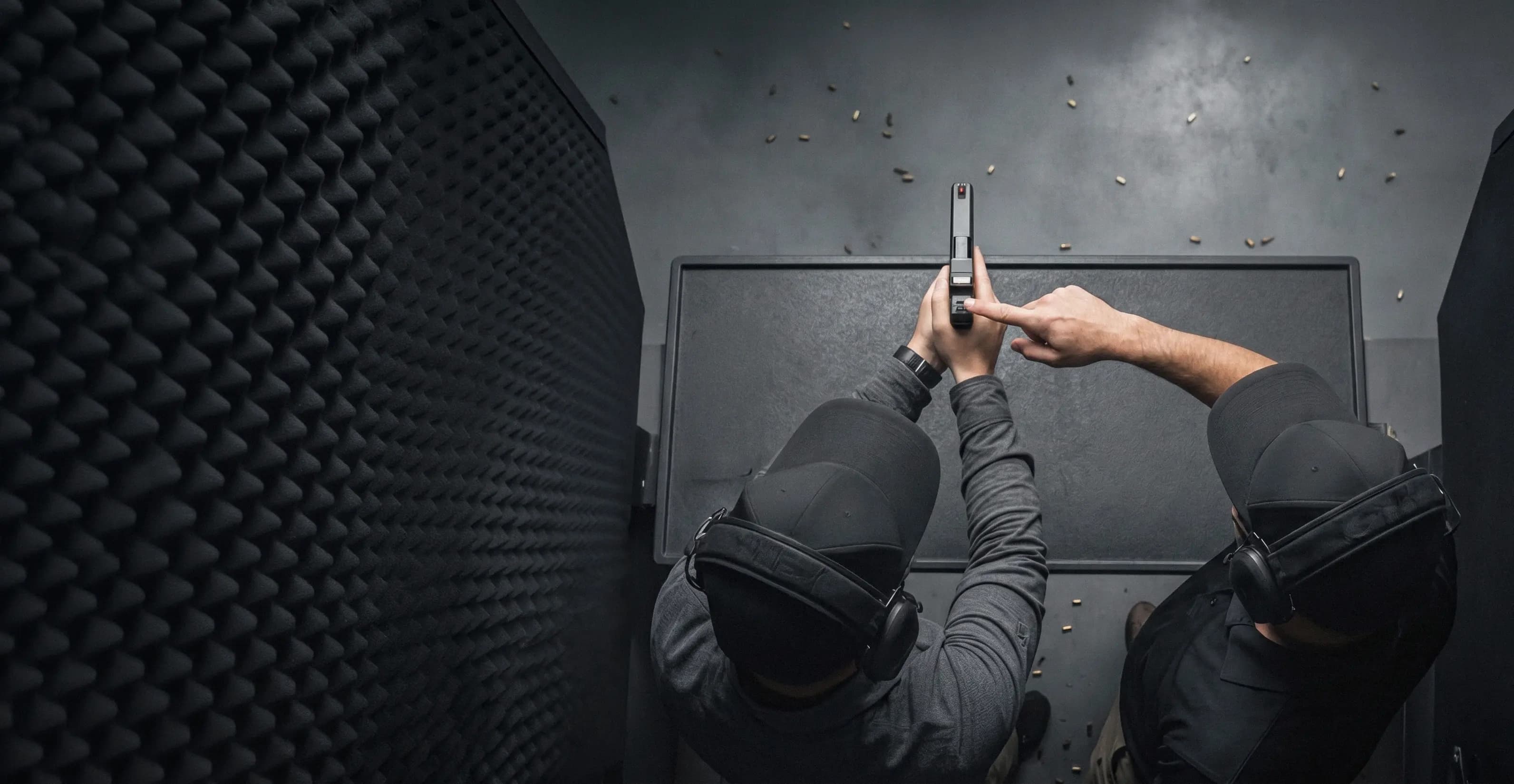 Overhead view of an instructor correcting a trainee's grip on a handgun at an indoor range